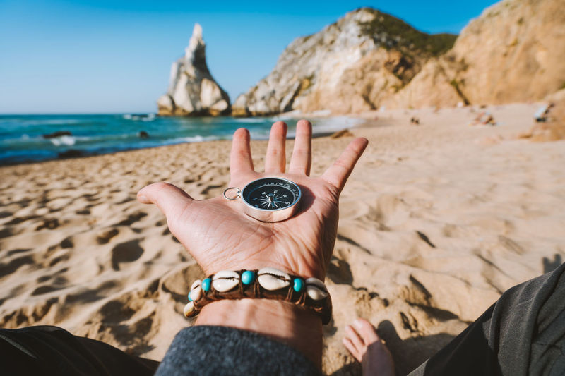 Close-up of hand holding navigational compass at beach