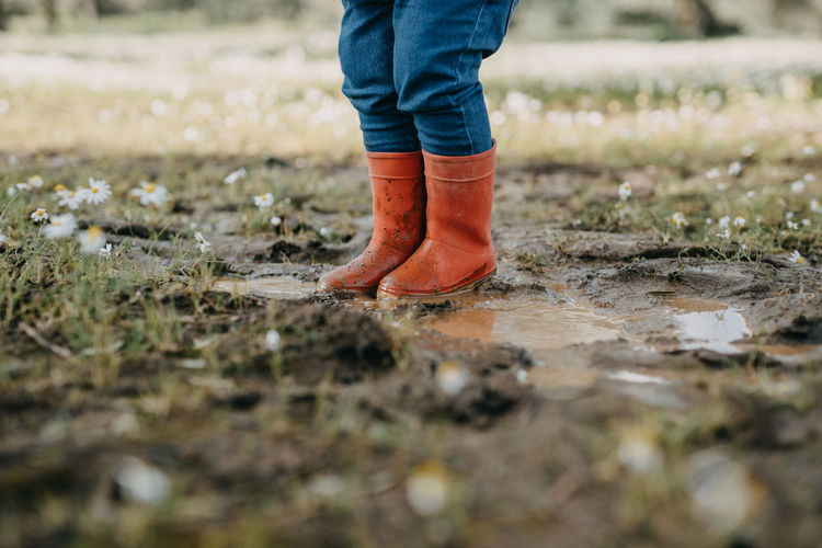 Low section of child standing in puddle with red rubber boots
