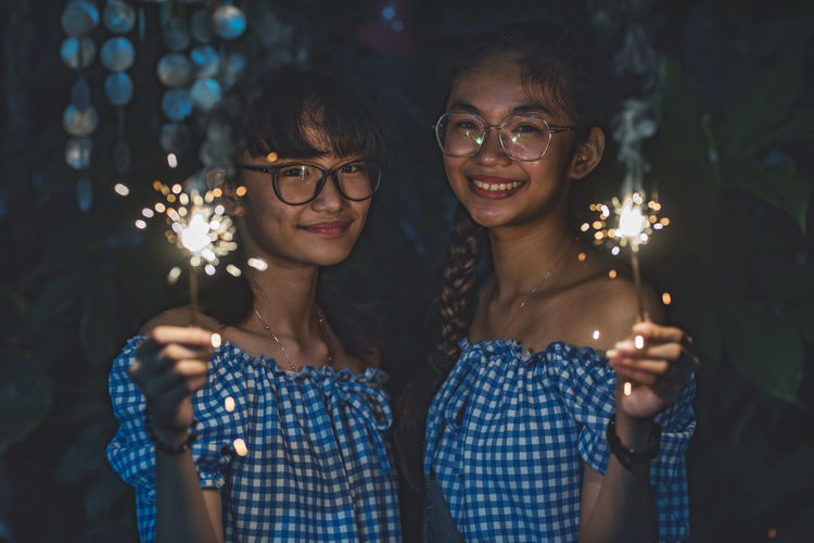 Portrait of smiling people holding sparklers at night