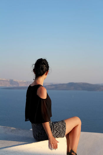 Rear view of woman sitting by sea against sky