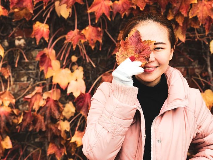 Portrait of young woman holding maple leaf during autumn
