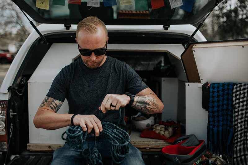 Man sitting on back of truck preparing rock climbing ropes