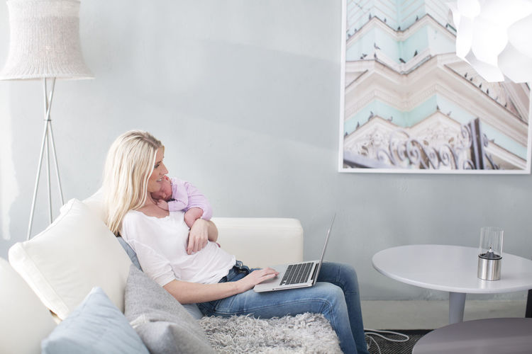 Woman holding newborn daughter and using laptop