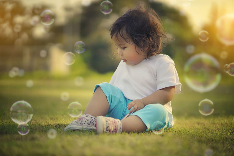 Girl playing with bubbles while sitting on field