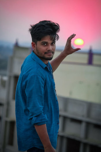 Portrait of young man holding sun while standing against sky