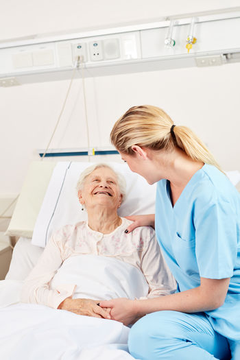 Smiling doctor consoling woman on bed at hospital