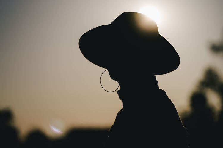 Close-up of silhouette woman wearing hat during sunset