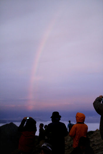 Rear view of people standing against rainbow in sky
