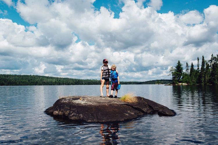 Low angle view of boys standing on rock in lake