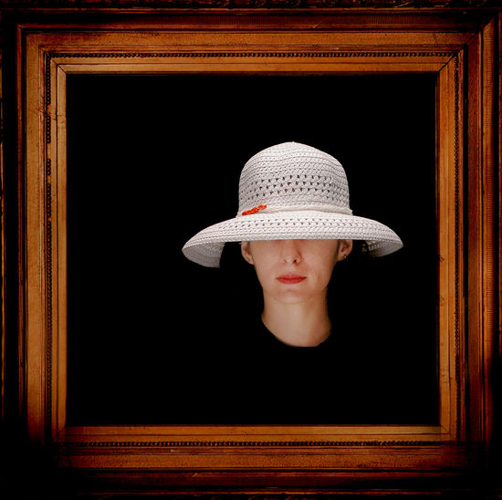 Woman wearing white sun hat seen from wooden picture frame against black background