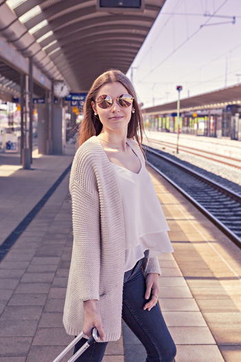 Portrait of young woman with luggage waiting at railroad station platform