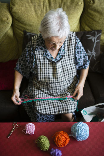 Senior woman crocheting on the couch at home, top view