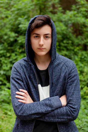 Portrait of boy wearing hoodie standing against trees