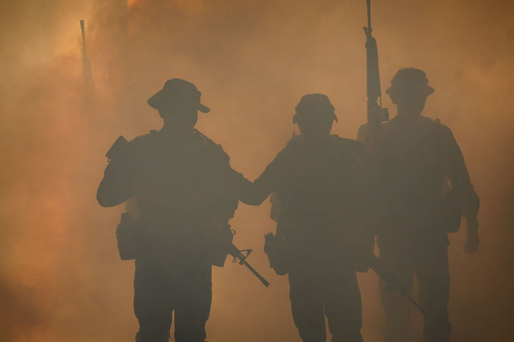 Silhouette army soldiers walking against smoke at night