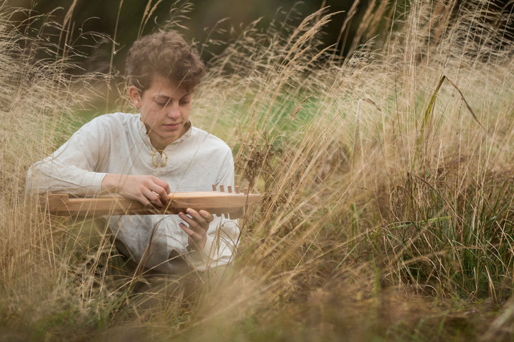 Teenage boy playing musical instrument on grassy field