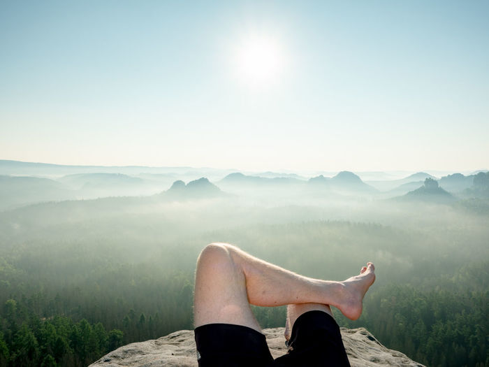Barefoot male body in black pants sleeps on cliff. morning fog. natural park in sachsen, deutschland