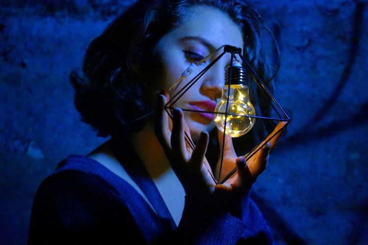 Teenage girl holding illuminated light bulb at night