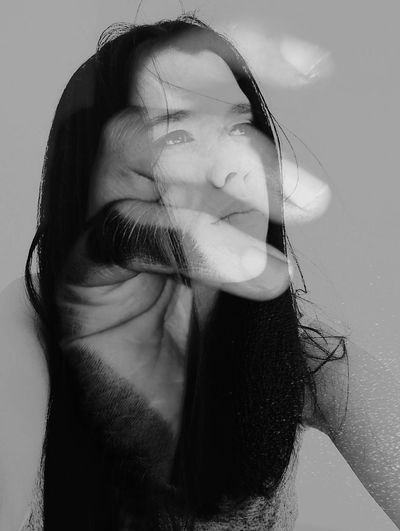 Double exposure of young woman and hand against gray background