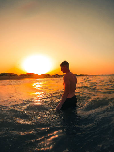 Man standing on sea against sky during sunset