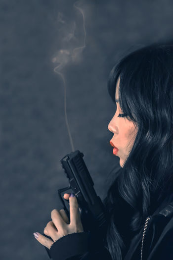 Side view of woman holding gun with smoke