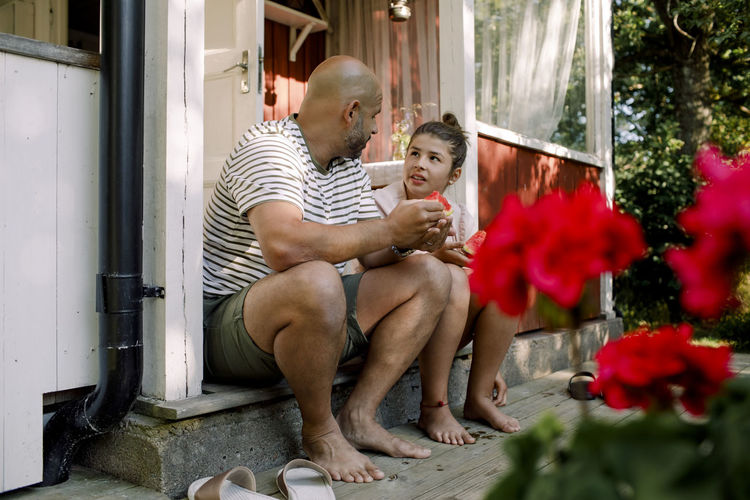 Father talking to daughter while eating slice of watermelon outdoors