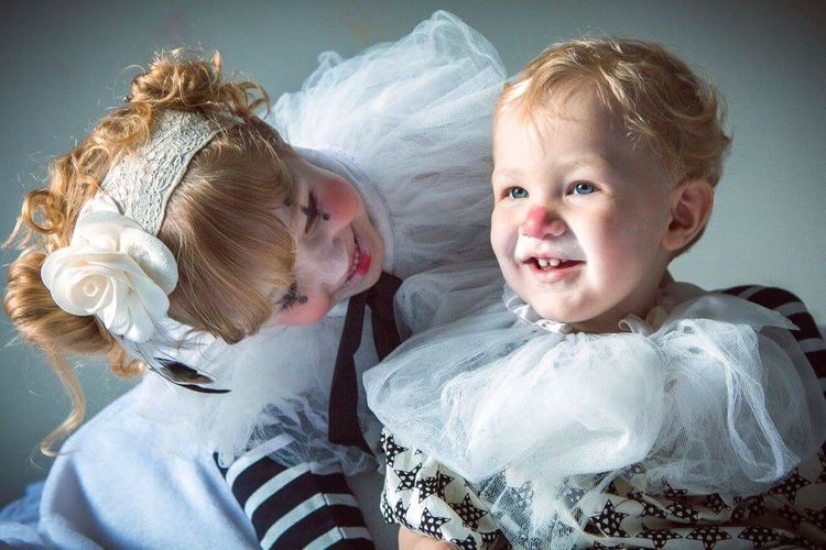 Cute siblings smiling in clown costume against colored background