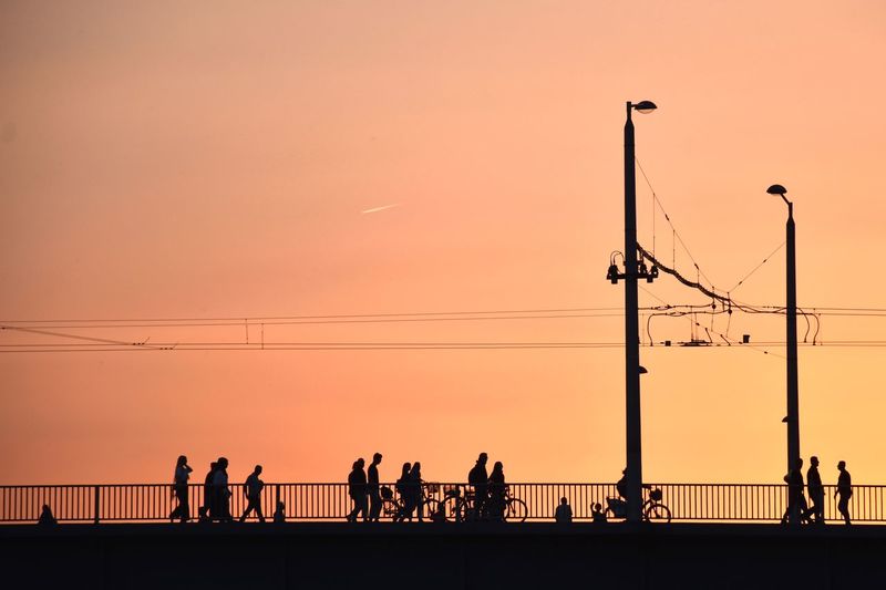 Silhouette people on bridge against sky during sunset