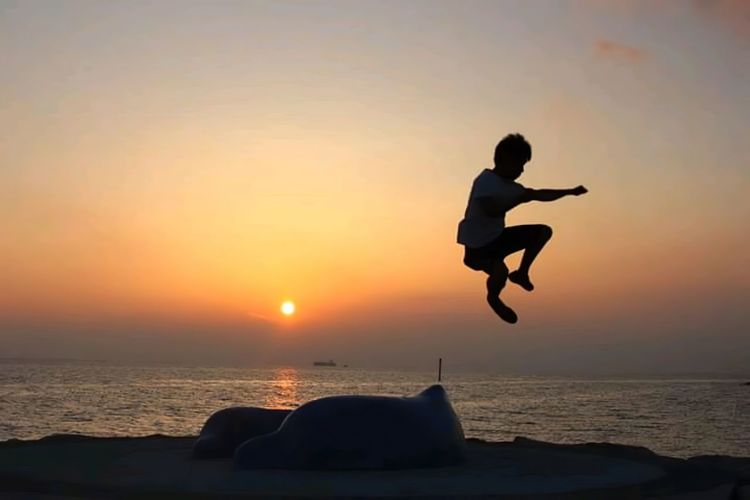 Silhouette man jumping in sea against sky during sunset
