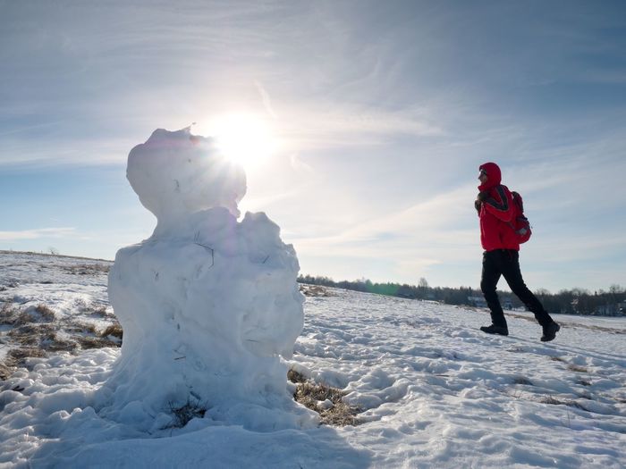 Real icy snowman standing in winter landscape. hot spring sun and some people walk at horizon