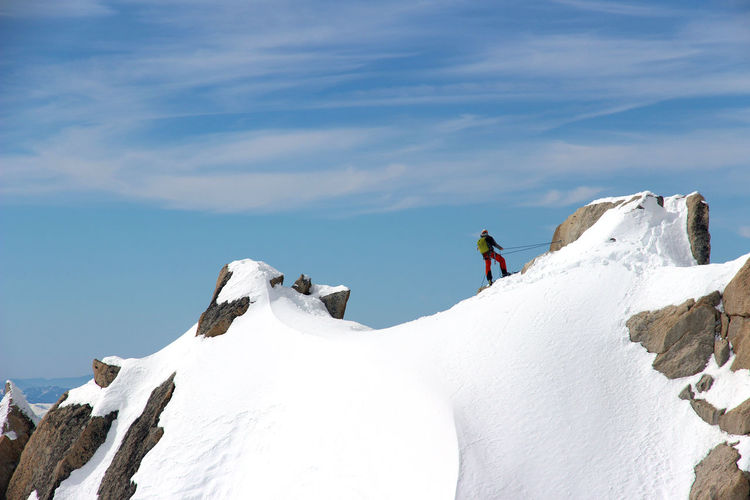 Man skiing on snow covered mountain against blue sky