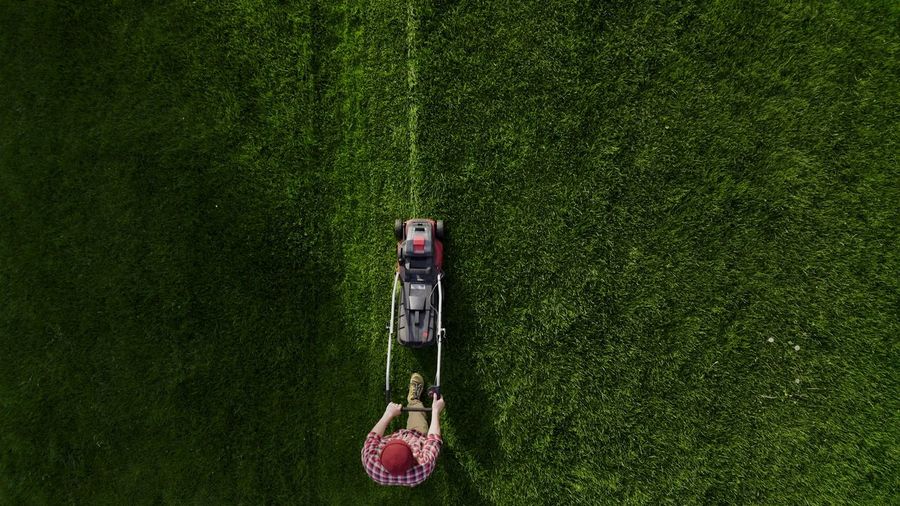 Top view of the lawn-mover worker cutting green grass garden