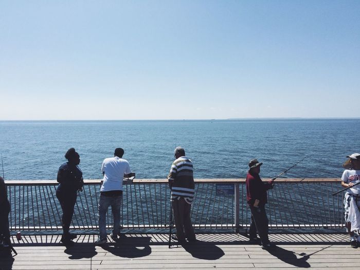 People fishing against railing by sea 