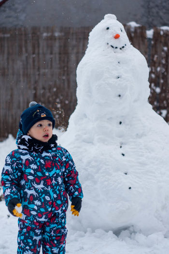 Cute boy standing against snowman