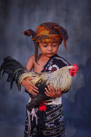 A little boy holding a rooster wearing indonesian traditional clothes 