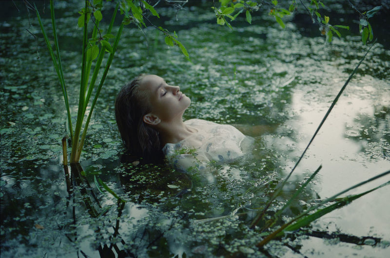 A woman in a white dress on the surface of a swamp water in the forest