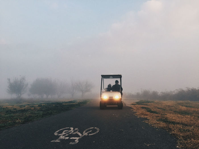 Father with son in golf cart on road amidst field during foggy weather