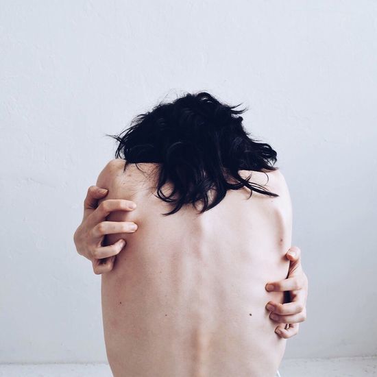 Rear view of naked woman hugging self against white wall