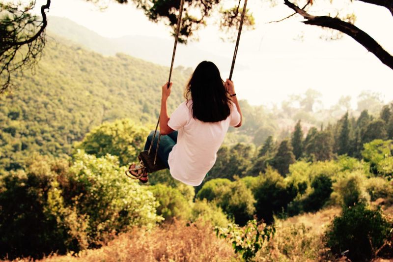 Rear view of woman on rope swing against mountains