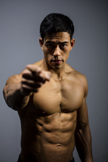 Portrait of shirtless muscular man pointing against wall