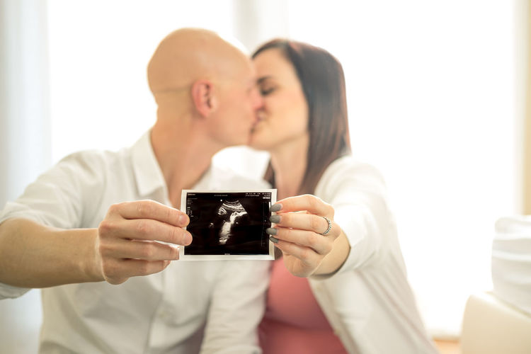Couple holding ultrasound photo while kissing at home