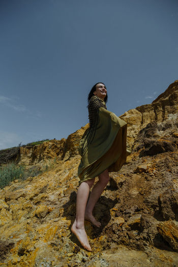 Side view of young woman on rock against sky