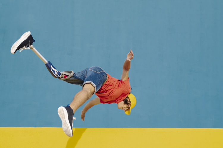 Man with artificial limb and foot jumping against multi colored wall