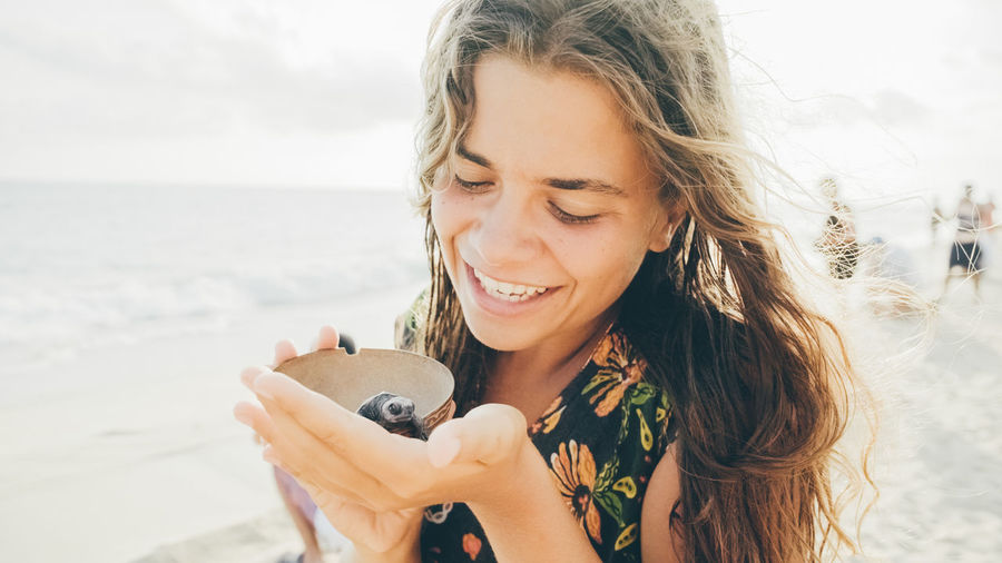 Portrait of smiling young woman holding sunglasses at beach