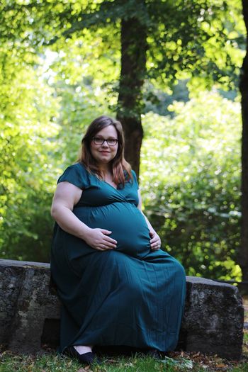 Portrait of smiling pregnant woman sitting against trees