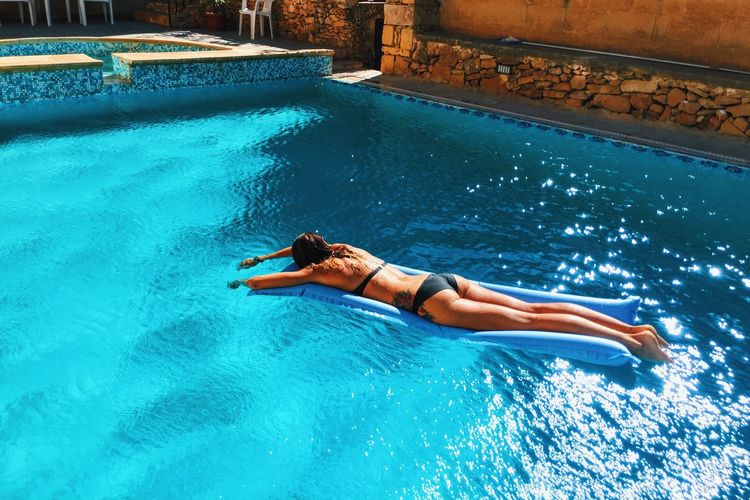 High angle view of sensuous woman in bikini relaxing on raft at swimming pool