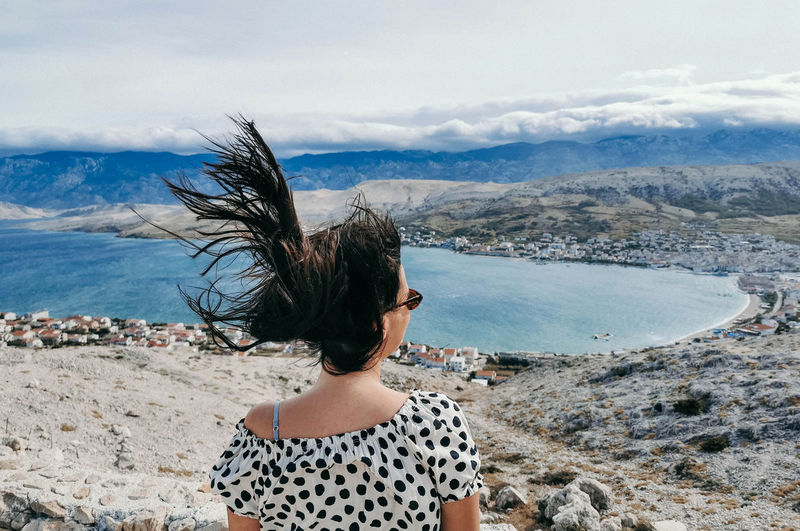 Rear view of young woman on viewpoint over sea. wind blowing hair.