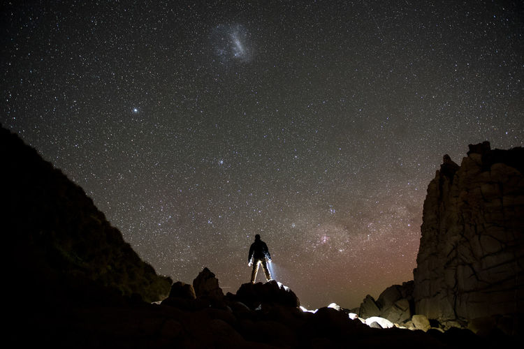 Silhouette man standing on rock against star field at night
