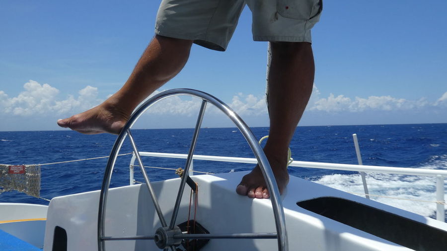 Low section of man standing on boat in sea against blue sky