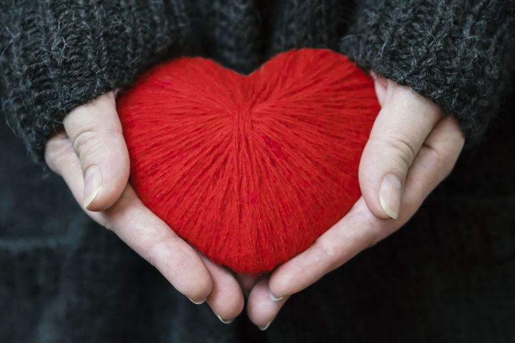 Close-up of hand holding red heart shape woolen yarn