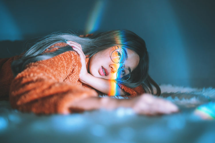 Woman lying down on bed with rainbow on face